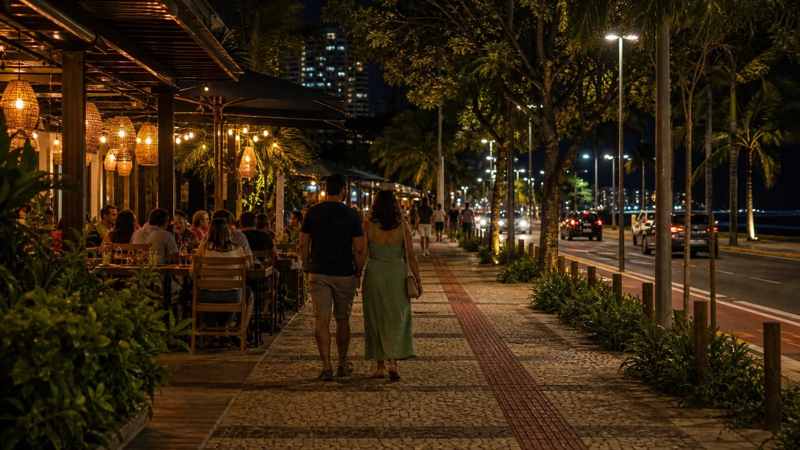 Rua iluminada em Vila Velha a noite com mesas vistas de longe e pessoas de costas