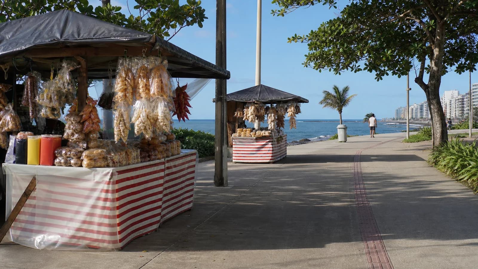 Bancas de produtos locais em Guarapari perto da orla, com mar ao fundo